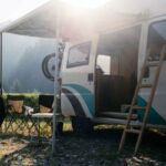 Vintage camper van parked on campground or camping in forest. Beautiful sunny morning in wild camp spot. Nomadic vanlife lifestyle. Relaxed simple vacation. RV camping destination