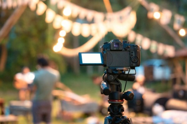 Camera recording standing on tripod with defocused illuminated live music concert event and camping background