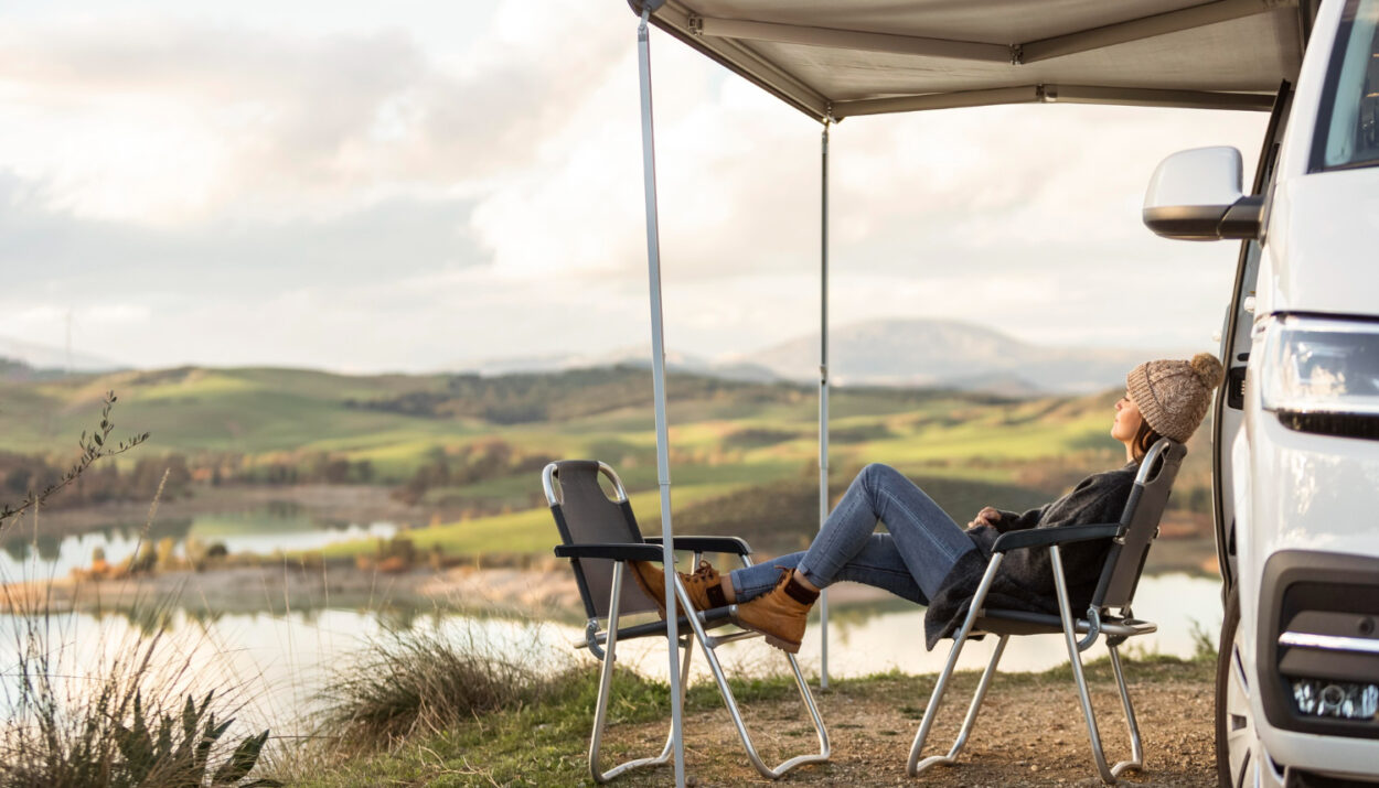 Woman with grey caridgan and jeans relaxing in front of a lake in a campground