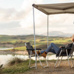 Woman with grey caridgan and jeans relaxing in front of a lake in a campground