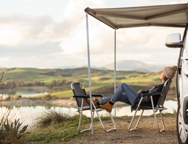 Woman with grey caridgan and jeans relaxing in front of a lake in a campground