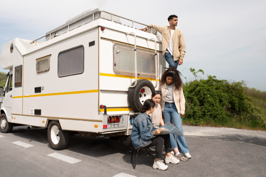 Group of friends outside of a white with yellow stripes camper looking for their next campground stay