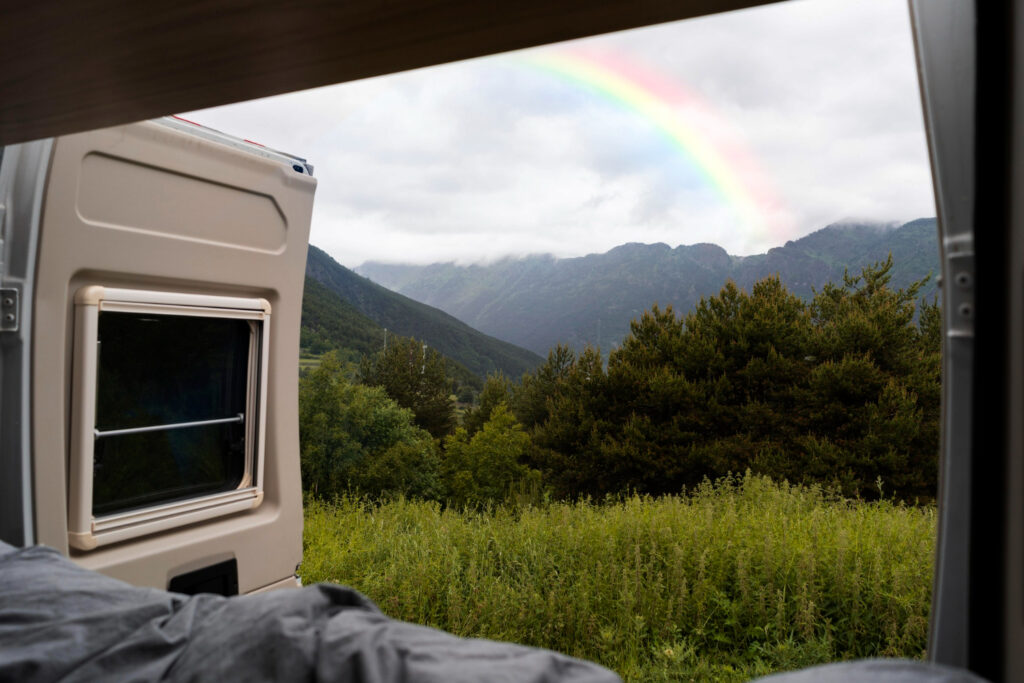 A beautiful view of the mountains with a rainbow from inside the camper in a campground