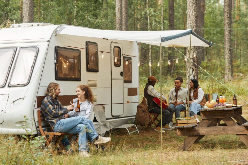 A group of friends enjoying a day in nature outside of a white camper by using a campsite booking software