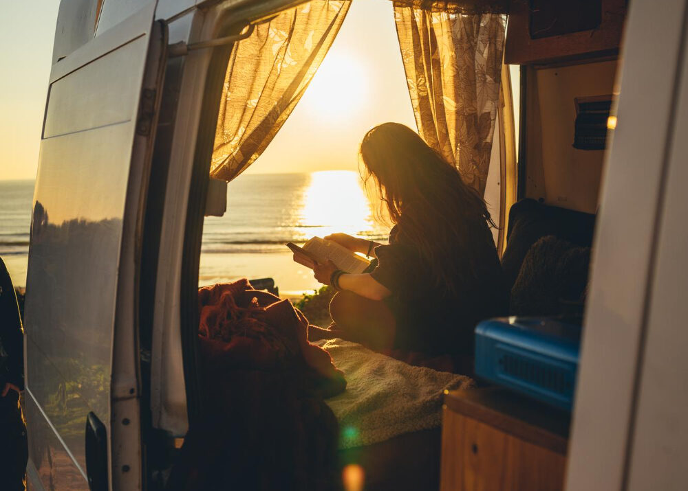 Woman enjoying a beautiful view inside of a camper in front of the beach