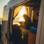 Woman enjoying a beautiful view inside of a camper in front of the beach