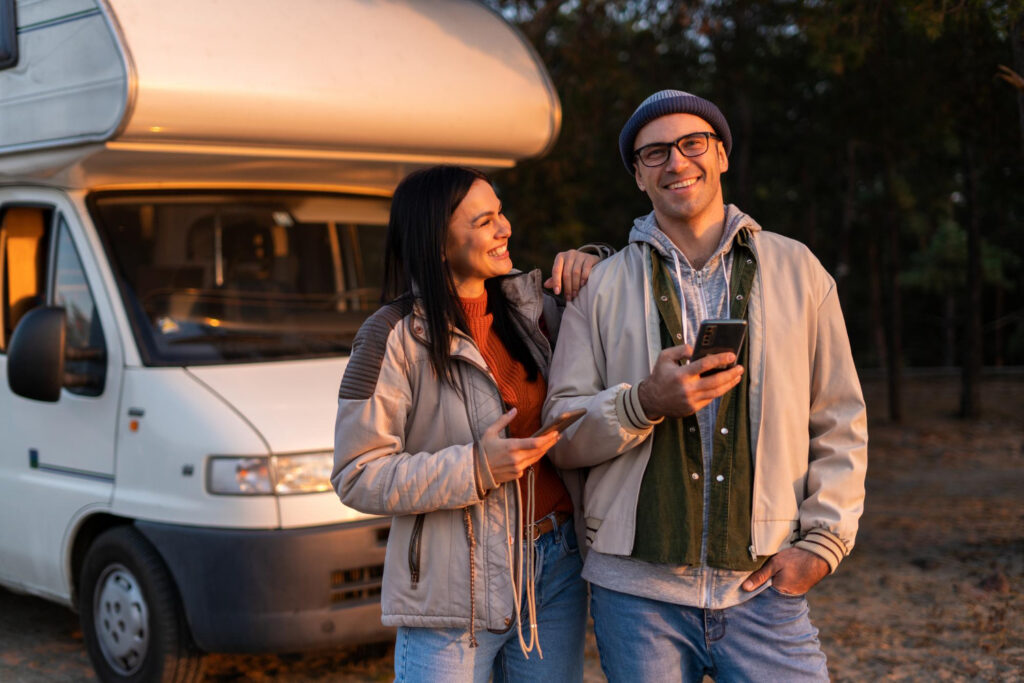 A woman and a man holding their phones in front of a camper van