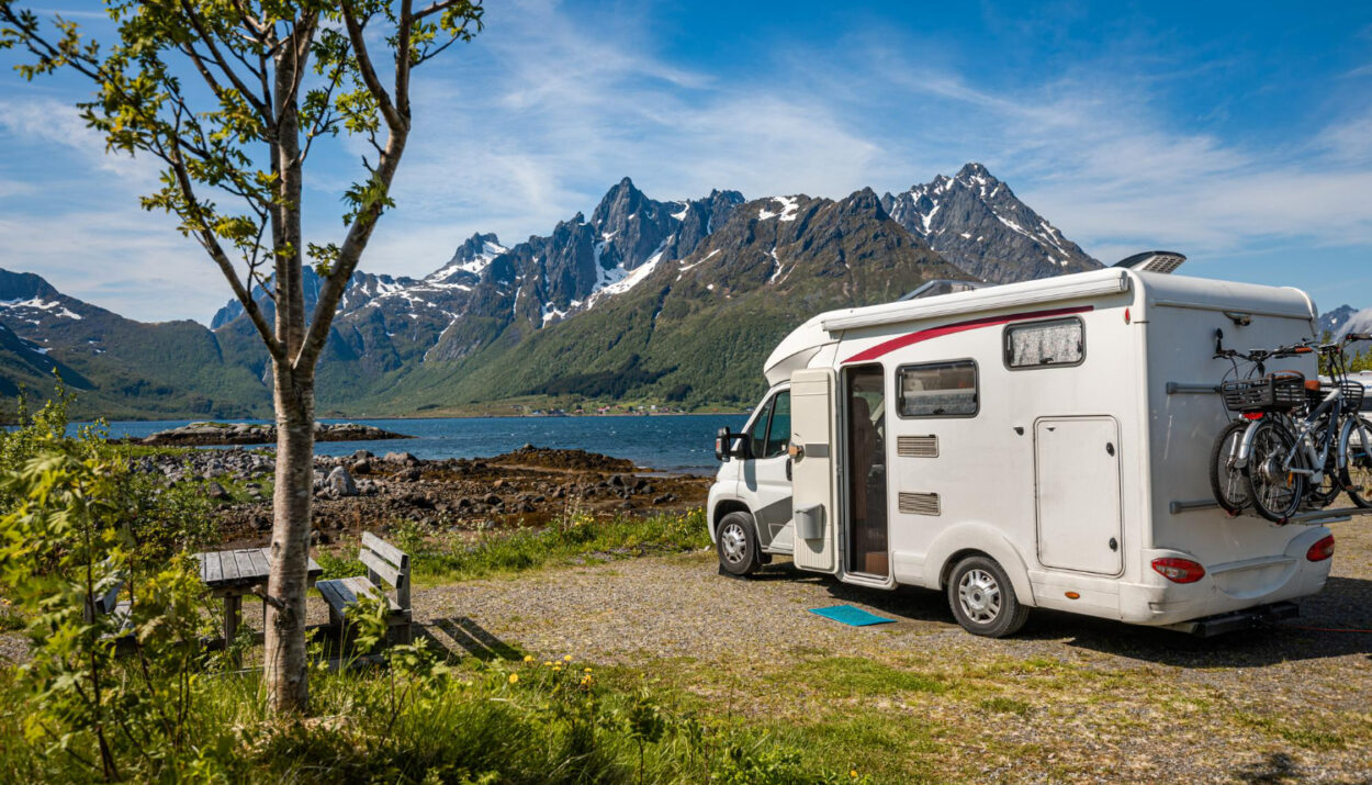 A white camper van in front of a lake with the mountains