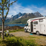 A white camper van in front of a lake with the mountains