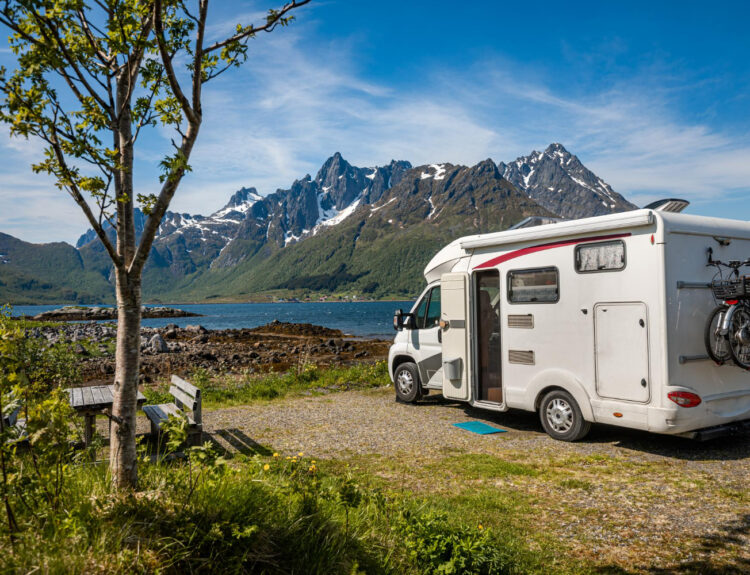 A white camper van in front of a lake with the mountains