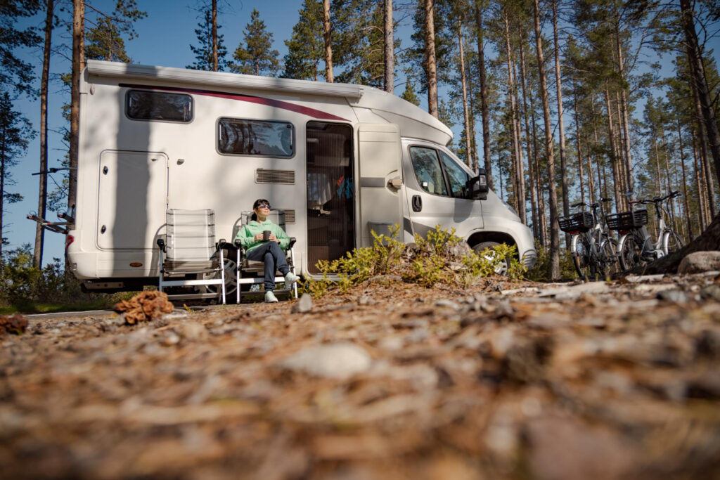 a woman in a green sueter enjoying a nature in a forest outside of a camper van