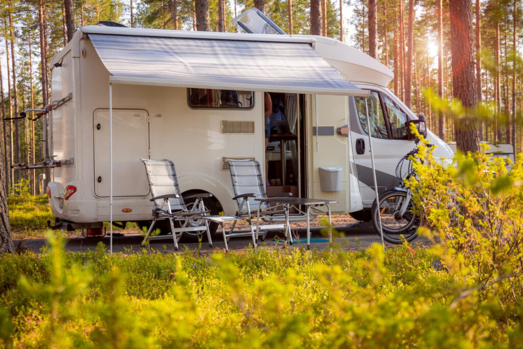 A white and grey camper with two chairs and a table outside in the nature 