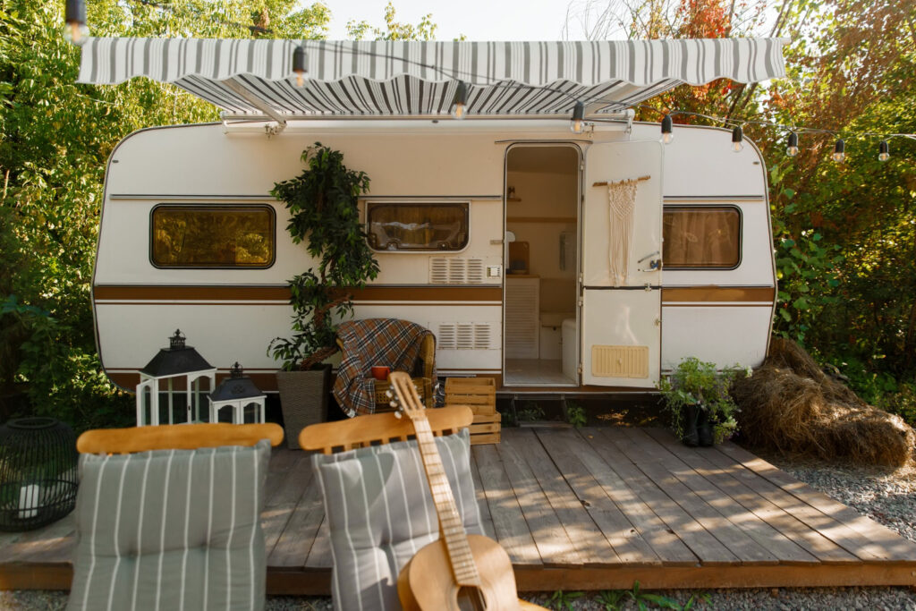 A white and brown camper van with a little porch and a few chairs in the forest 