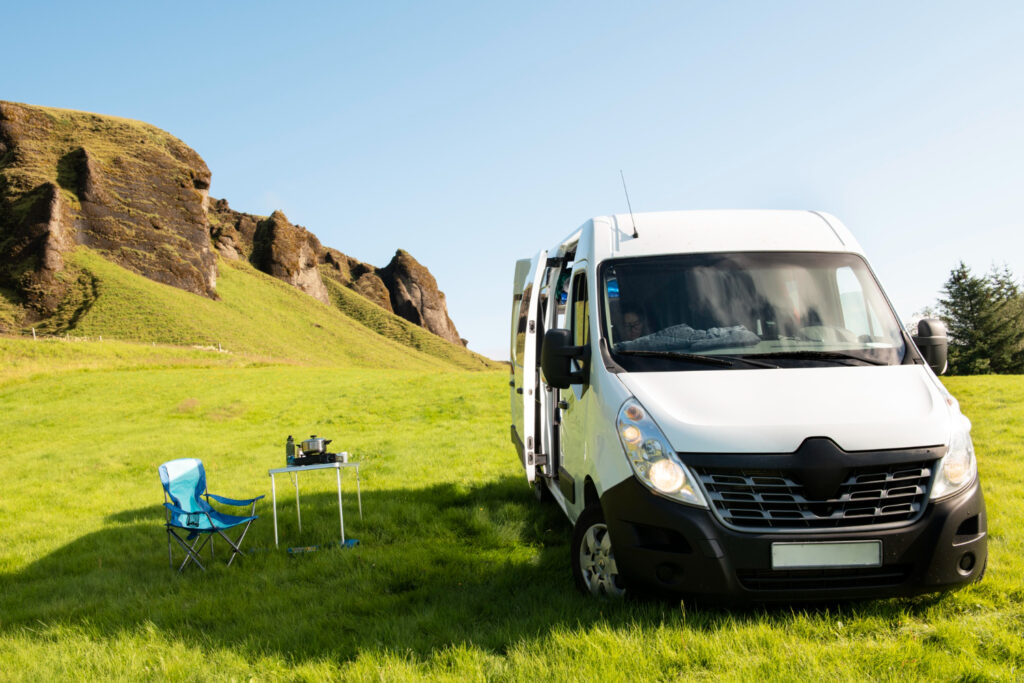 a camper with the doors open in the mountains with one chair and a table 