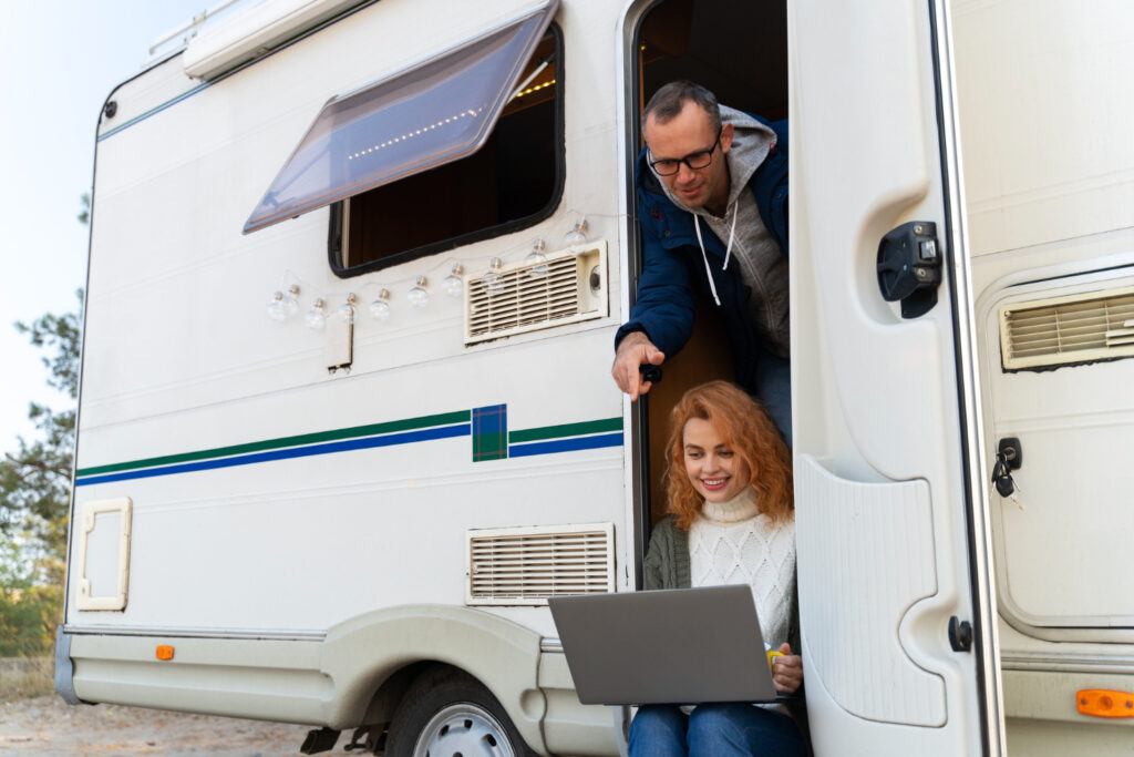 a woman and a men with a blue jacket inside a white with blue and green stripes camper van checking in a laptop the best camprgound management software