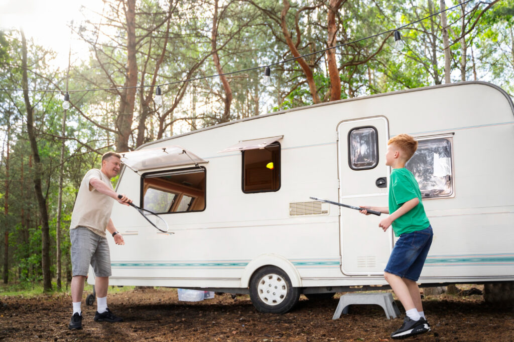 A father and a son playing badminton outside of a camper van in a campground spot