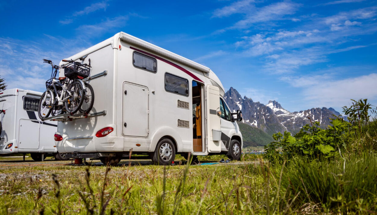 A white camper with bikes attached in the back with mountains in front of it