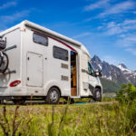 A white camper with bikes attached in the back with mountains in front of it