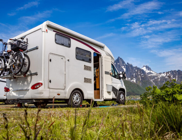 A white camper with bikes attached in the back with mountains in front of it