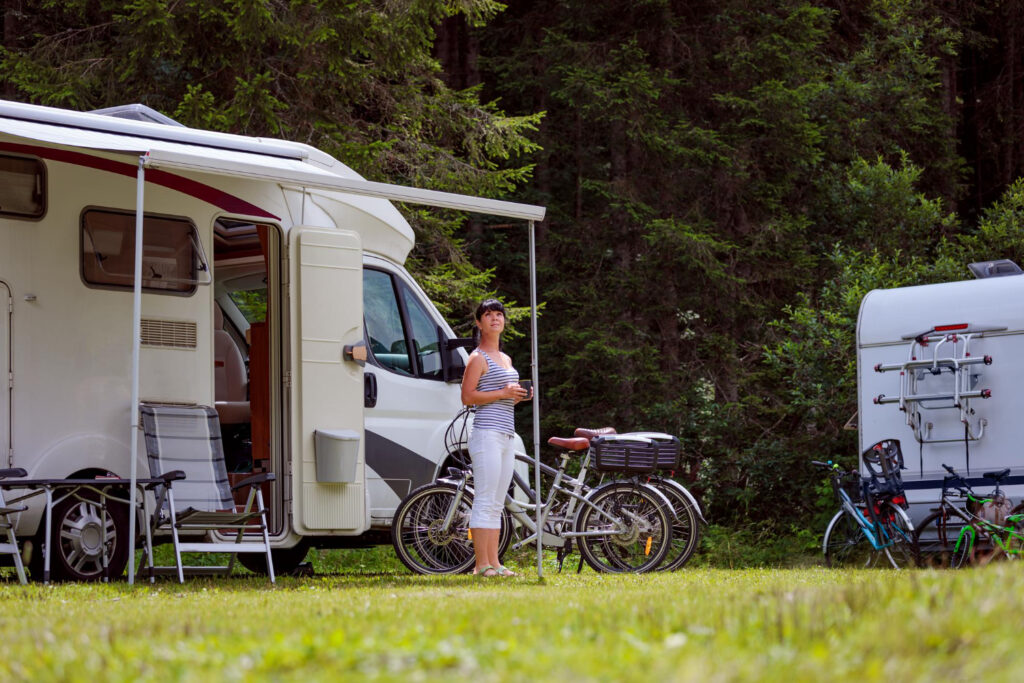 A woman standing in front of her camper can enjoying a cup of coffee in an RV park