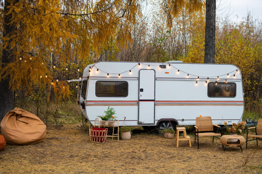 a white with red, brown and blue stripes camper van with a few lights hanging in their RV park spot