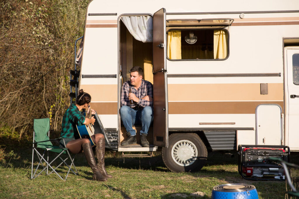 Two people playing music in a beige and brown camper outside in the nature 