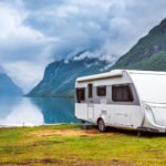 A white camper van in front of a lake with mountains