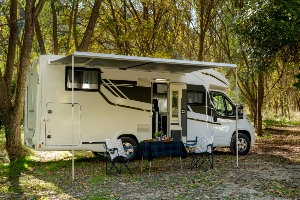 A white and grey camper van in nature with two chairs and a table set up 