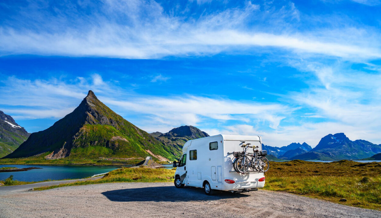 A white campground with two bikes attached behind it and mountains in front of it