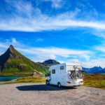 A white campground with two bikes attached behind it and mountains in front of it