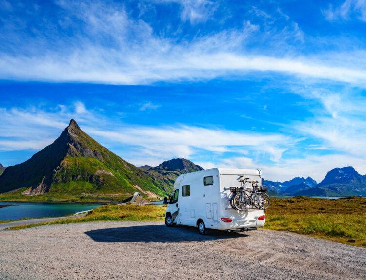 A white campground with two bikes attached behind it and mountains in front of it