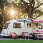 a white camper van in the forest with a beautiful sunset behing and red chairs