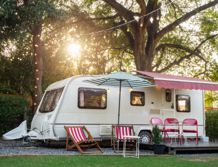 a white camper van in the forest with a beautiful sunset behing and red chairs