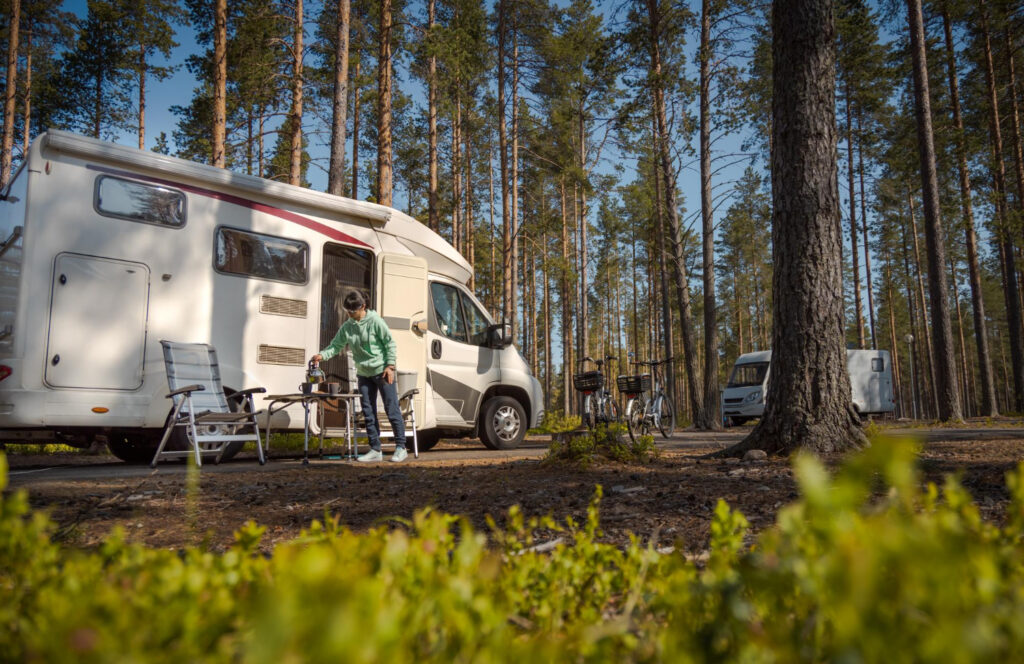 A woman in a green sueter outside of her camper van enjoying a cup of coffee in nature 