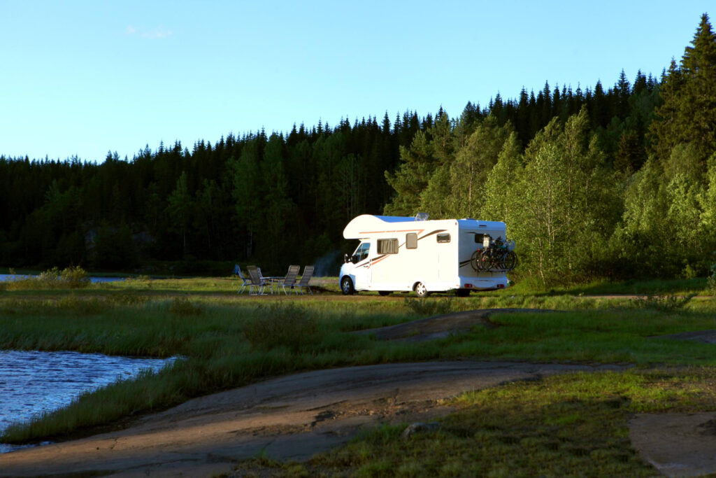 A camper with a few bikes attached to it sited in front of a lake in the forest thanks to campsite management software