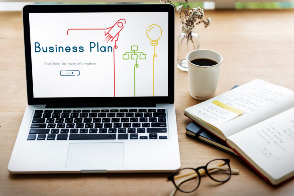 a laptop with the word business plan an a coffee cup and a notebook