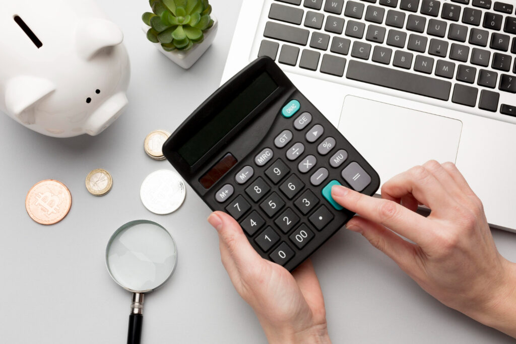 A person using a calculator with a laptop on the side