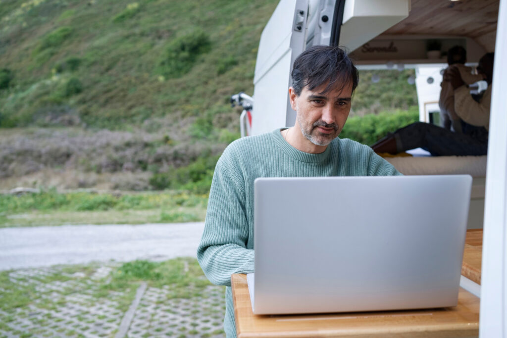 a man using his laptop outside of a campground to check his camping reservation software 