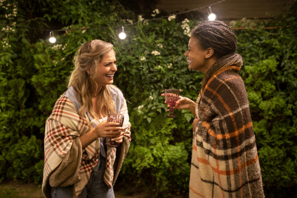 two women with blankets and glasses having a good time in a campground 