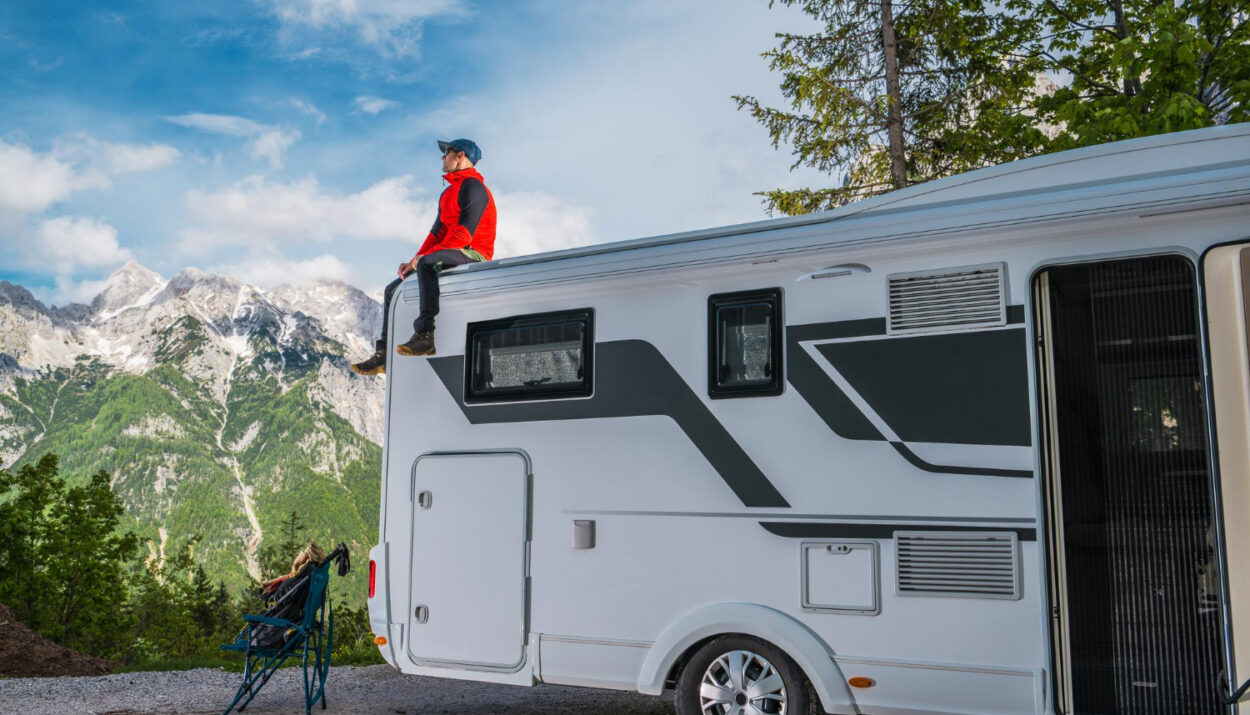 A man sitting a the top of his camper van with the mountains in front of him