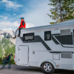 A man sitting a the top of his camper van with the mountains in front of him