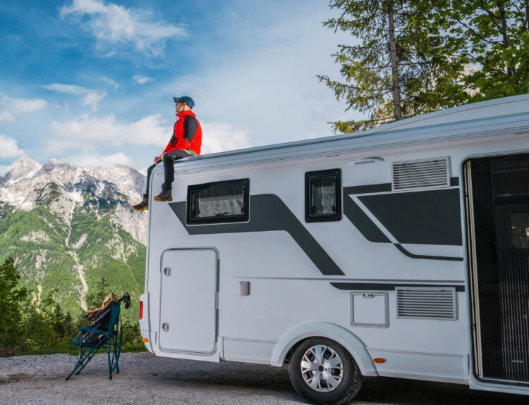 A man sitting a the top of his camper van with the mountains in front of him