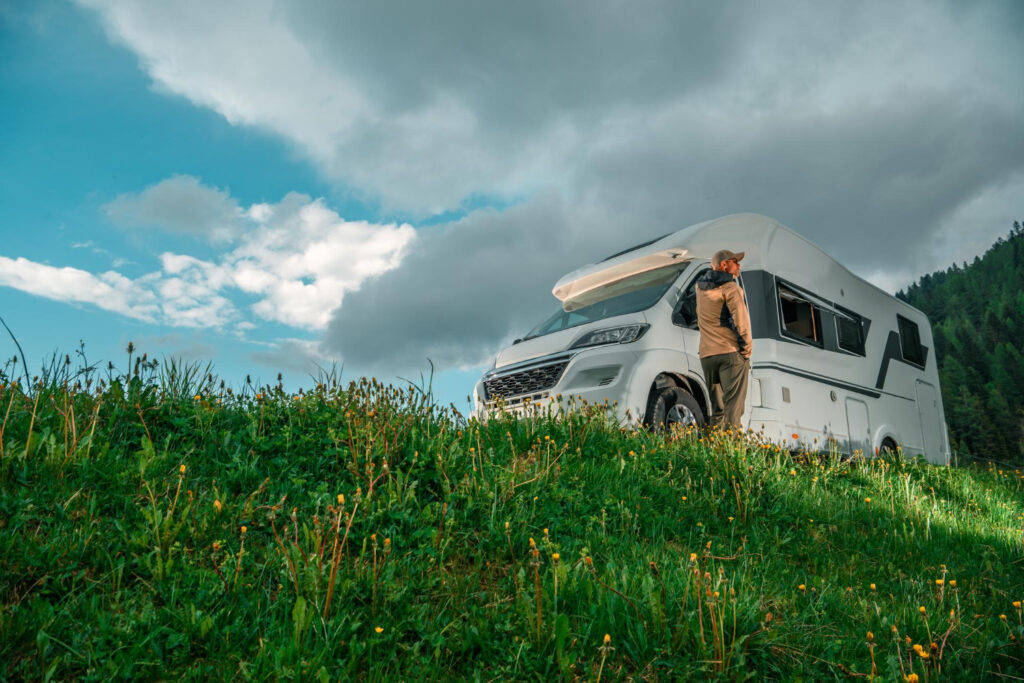 a man in front of his camper van in a low point of view with vlouds and the green grass