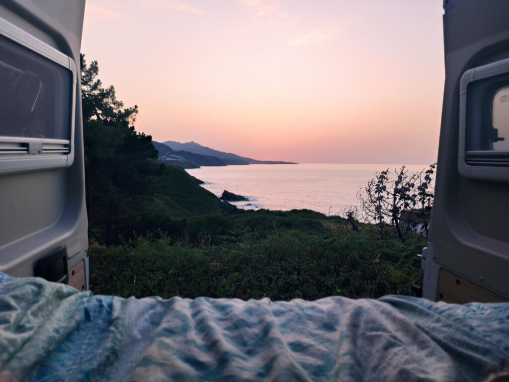 an inside view of a camper van with the beach in front of it with the sun rising 