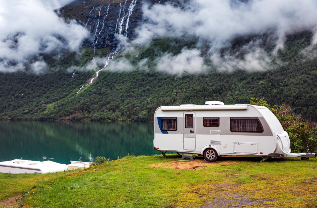 A white camper with a blue line in the mountains with the partial view of a lake