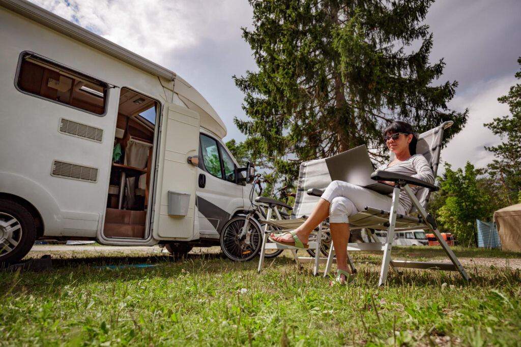 A woman using her laptop outside of her camper van using campground reservation software 