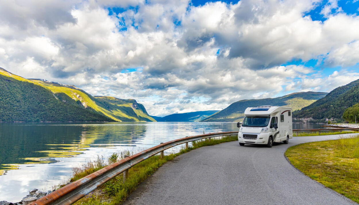 A white camper van on the road with a view of a lake behind it