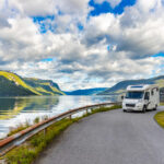 A white camper van on the road with a view of a lake behind it