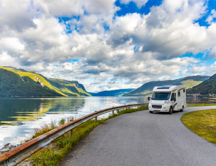 A white camper van on the road with a view of a lake behind it