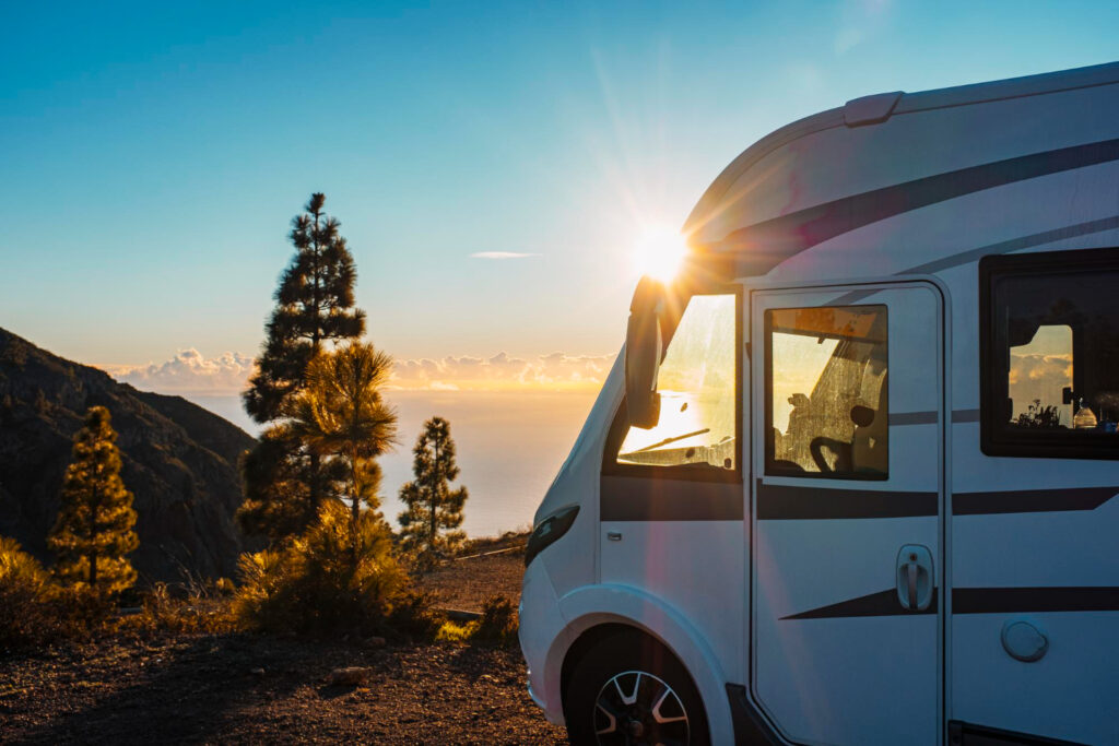 A white and grey camper van in front of a mountain with the sun rising 